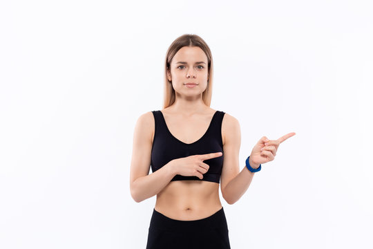 Young sporty blond woman in a black sportswear with smart watches for pulse measuring pointing with fingers to the right.