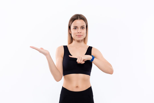 Young sporty blond woman in a black sportswear with smart watches for pulse measuring pointing with one hand at the pulm of a hand