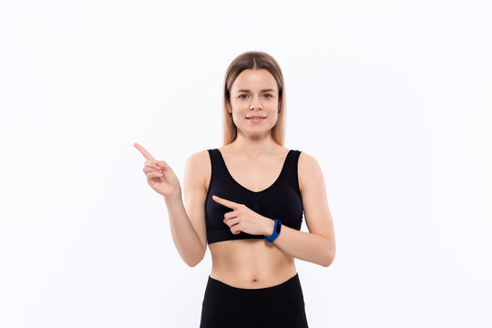Young sporty blond woman in a black sportswear with smart watches for pulse measuring pointing with fingers to the left.