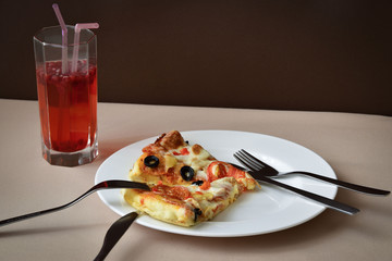 A slice of pizza on a white plate with two sets of eating utensils. A single glass of fruit drink with two straws. © Кристина Исаченко
