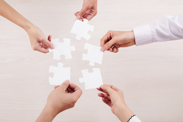 Close-up of team connecting their puzzles and demonstrating unity of friendship isolated on white background