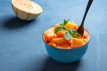Fresh melon cut into pieces in a bowl and background blue - image