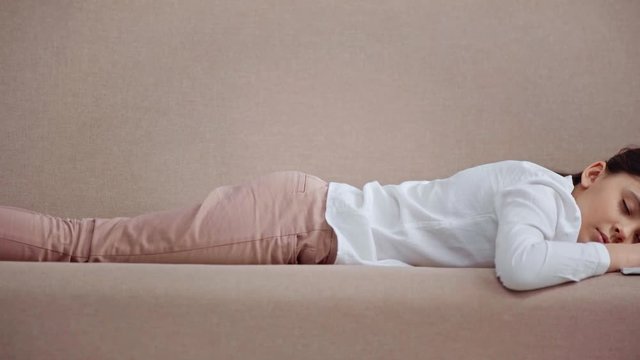 tired preteen schoolgirl lying on sofa and sleeping next to copy book and book