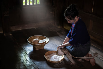Young woman sit on coconut grater and grate coconut into bowl.