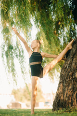 Girl gymnast stands in a twine pose in the park.