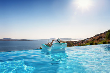 Attraktive Frau im Bikini treibt auf einer Luftmatratze im Pool und genießt die Aussicht auf das...