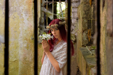 A young woman is trapped inside a jail ruin. She is  dressed in white and wears a thorn wreath on...
