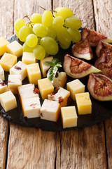 Cheese in assortment with grapes and figs close-up on a slate board. vertical
