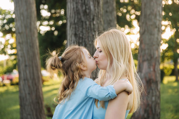 Young beautiful woman with her little cute daughter. Young daughter hugs mother in summer park....