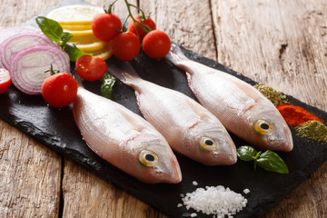 Fresh raw dorado or gilt-head sea bream fish with spices, tomatoes, onions and lemon closeup on a slate board. horizontal