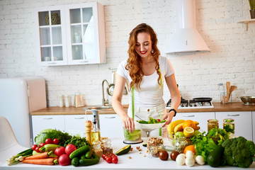 Young happy woman preparing tasty salad in the beautiful kitchen with green fresh ingredients indoors. Healthy food and Dieting concept. Loosing Weight