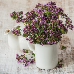 Fresh flowering oregano grass (Origanum vulgare) and a small teapot on the old table. Selective focus.