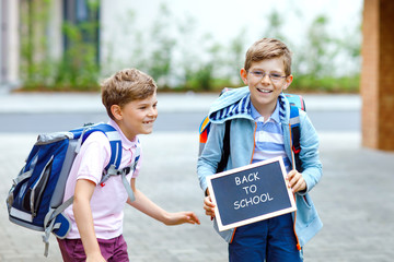 Naklejka premium Two little kid boys with backpack or satchel. Schoolkids on the way to school. Healthy children, brothers and best friends outdoors on street leaving home. School's out on chalk desk. Happy siblings.
