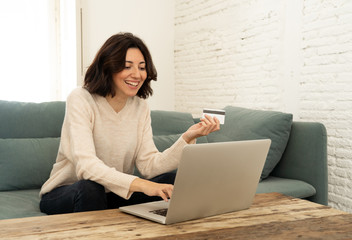 Happy young woman sitting with laptop and a credit card shopping online at home