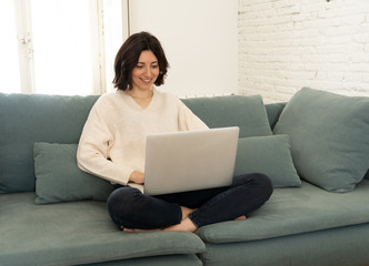 Naklejka premium Happy young woman working on her laptop sitting cross-legged on the sofa. In technology concept