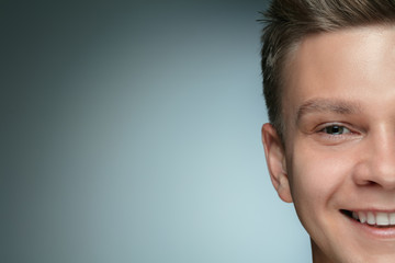 Close-up portrait of young man isolated on grey studio background. Caucasian male model looking at camera and posing, smiling. Concept of men's health and beauty, self-care, body and skin care.