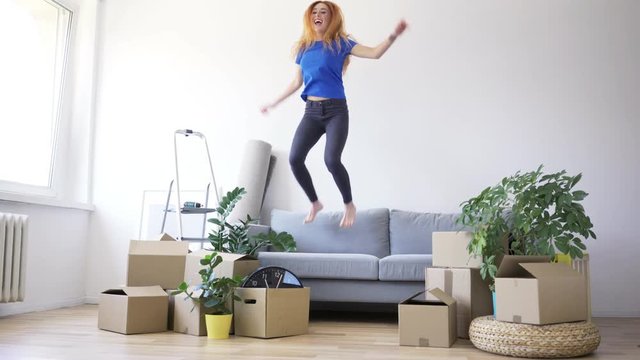 Joyful Young Woman Jumping On Sofa After Moving To New Apartment