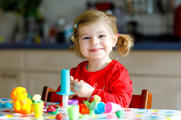 Adorable cute little toddler girl with colorful clay. Healthy baby child playing and creating toys...