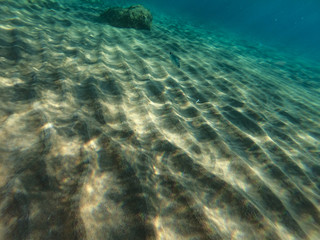 Underwater view of the rocks, sand and stones. The sandy and rocky bottom of the sea with some sun rays.