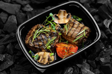 Well done beef steak with vegetables in black take away box
