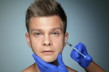 Close-up portrait of young man isolated on grey studio background. Filling surgery procedure. Concept of men's health and beauty, cosmetology, self-care, body and skin care. Anti-aging.