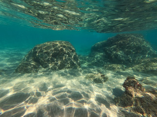 Underwater view of the rocks, sand and stones. The sandy and rocky bottom of the sea with some sun rays.