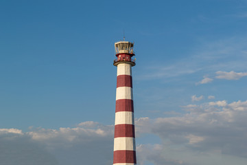 Lighthouse on the beach on a Sunny day against the blue sky.  Trees grow near the lighthouse.