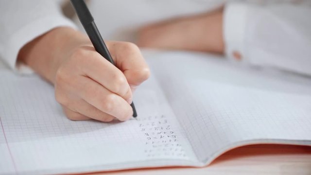 cropped view of schoolgirl in white shirt doing math homework and checking answers in copy book