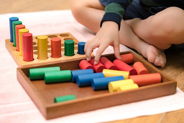 Closeup: Hands of a little Montessori kid (3-6) learning about size, orders, sorting, arranging by engaged colorful wooden sensorial blocks. Educational toys, Cognitive skills, Montessori activity.