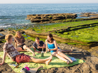 Group of young friends picnicking on rocky beach at Playa de Azkorri, Getxo, Basque Country, Spain