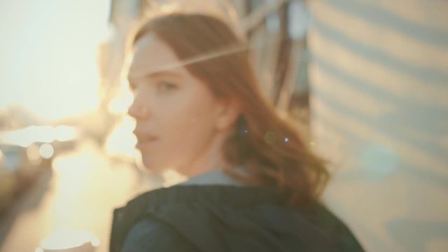 Young woman with red hair walking in the city streets. Turing around and looking into the camera.