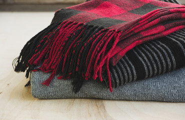 Warm clothes on a wooden table. Scarves and sweater in the stack. Concept: cozy, cold season. 