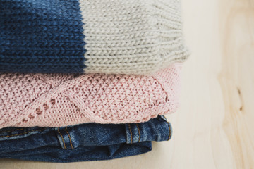 Warm clothes on a wooden table. Sweater, hat and jeans in the stack. Concept: cozy, cold season. Scandinavian style. 