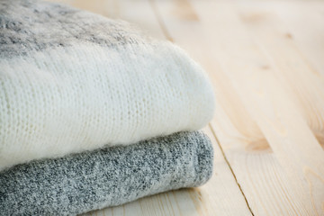 Warm clothes on a wooden table. Knitted sweaters in pastel colors. Concept: cozy, cold season. Scandinavian style. Copy space