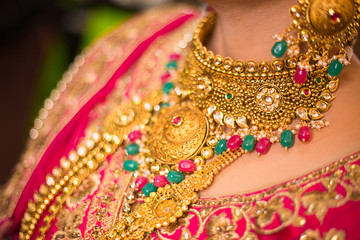 Indian bride wearing heavy jewellery traditional gold necklace, red green gem stone design,  fashion background 