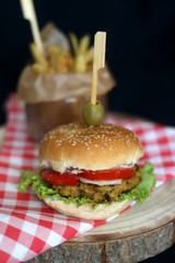 Homemade vegan burger made with chickpeas and zucchini, served with lettuce, tomato, cucumber, pickles and sauce. Fries on the side. Selective focus, dark background.