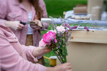 Female hands of florist creating summer modern bouquet of different flowers in pink purple colors in shop