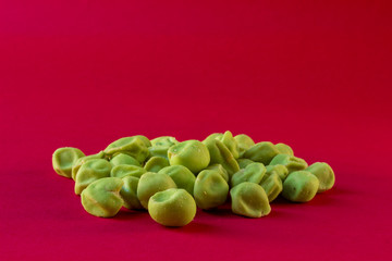 close up of wasabi coated peanuts on a red background