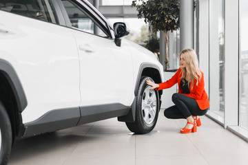 Woman sitting next the white car and touching a wheel.- Image