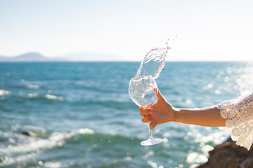 Splash of wine. Hand holding glass of rose vine on sea or ocean background. Top view, copy space....