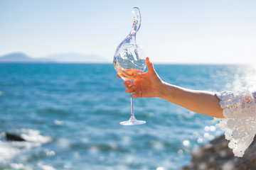 Splash of wine. Hand holding glass of rose vine on sea or ocean background. Top view, copy space....