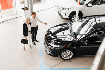 Family couple in dealership choose a car, man pointing to automobile. Top view