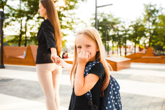 Mom Leads Her Daughter To School. Return To School. Woman And Girl With Backpack Behind The Back. Beginning Of Lessons. First Day Of Fall.