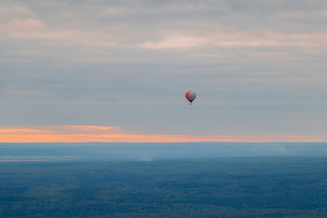 Colorful balloon high above the ground in the sky at sunset in fog