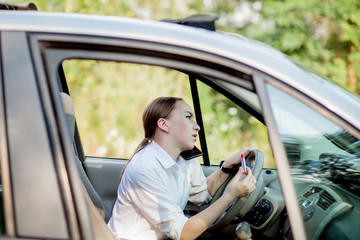 Picture of young businesswoman speaks by phone and doing makeup while driving a car in the traffic jam