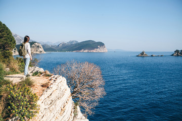 A tourist with a backpack on top of a cliff or hill next to the sea looks into the distance. Travel alone.