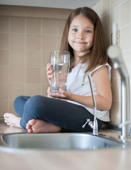 Portrait of a little caucasian baby girl holding a glass of tap clean water. Kitchen faucet. Cute...