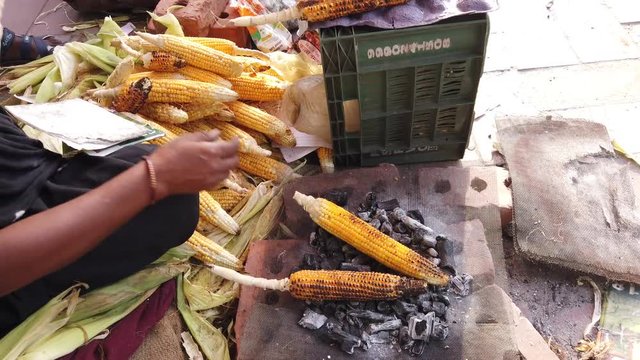 Corn on the cob, slow roasted over hot coals, with squeeze juicy lime wedges and sprinkle salt, cayenne pepper, spicy masala chaat. Popular street food in Southeast Asia. 4k 60fps handheld close-up