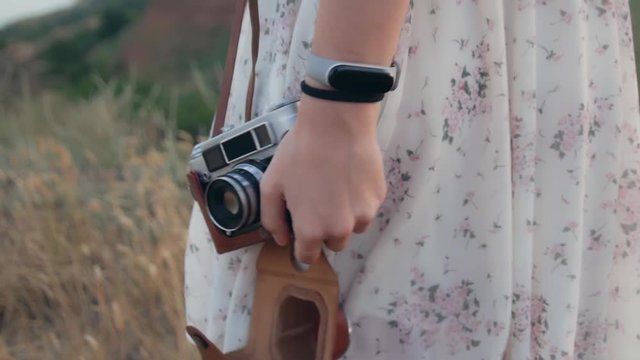 Young woman's hand raising the retro camera in a brown case to take a picture in a field on sunset. Close up, slow motion.
