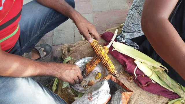 Corn on the cob, slow roasted over hot coals, with squeeze juicy lime wedges and sprinkle salt, cayenne pepper, spicy masala chaat. Popular street food in Southeast Asia. 4k 60fps handheld close-up